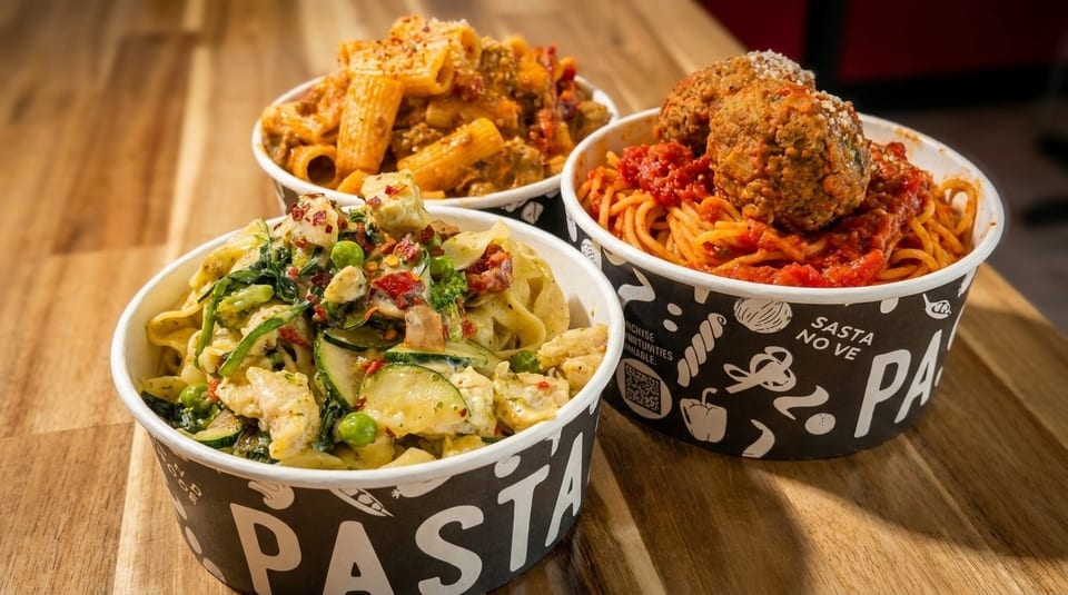 Three bowls of pasta on a wooden table: rigatoni with meat sauce, fettuccine with chicken and vegetables, and spaghetti with meatballs.