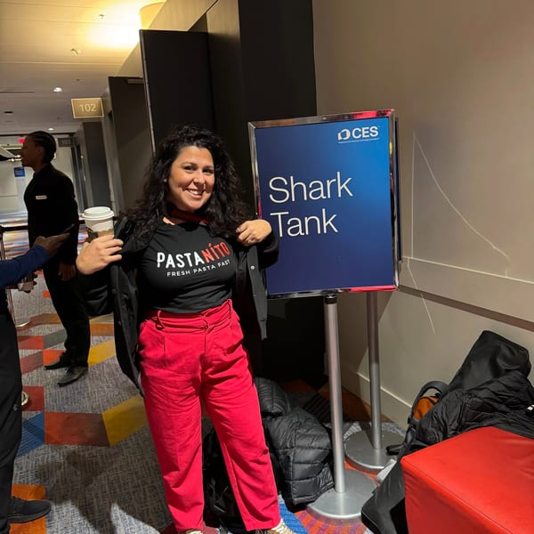 A woman in a "PASTANITO" shirt and red pants smiles next to a "Shark Tank" sign.