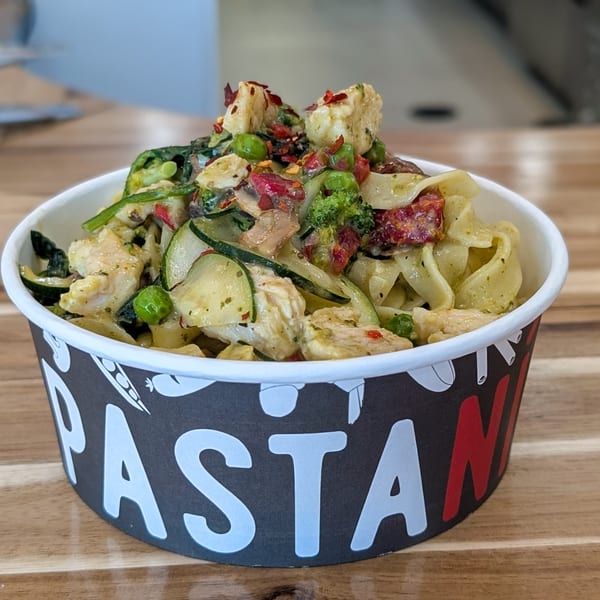 Pasta Mia bowl filled with fettuccine, chicken, zucchini, peas, broccoli, and sun-dried tomatoes.