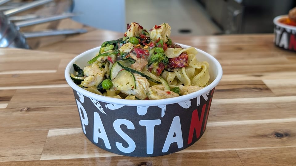 Pasta Mia bowl filled with fettuccine, chicken, zucchini, peas, broccoli, and sun-dried tomatoes.