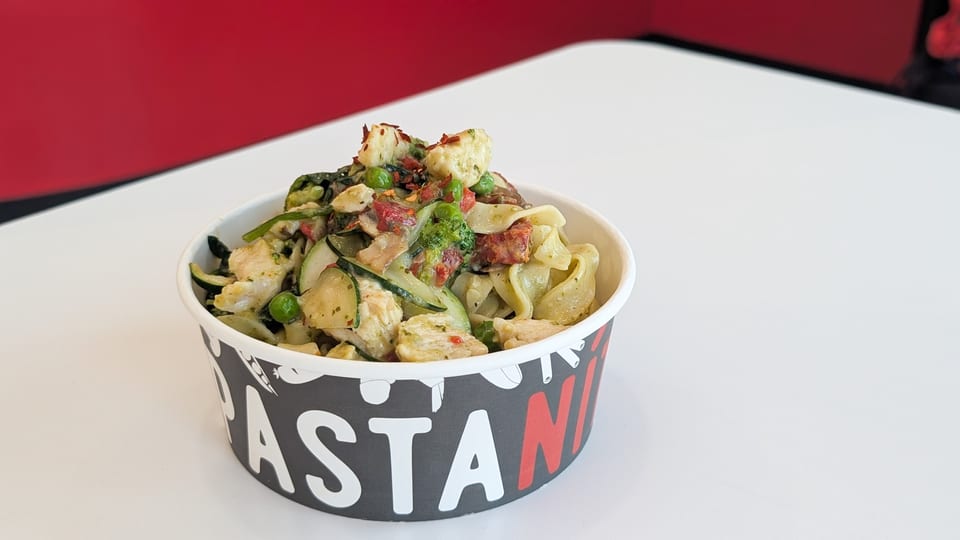 PastaMania's pesto pasta with chicken, zucchini, peas, and sun-dried tomatoes in a branded cup.