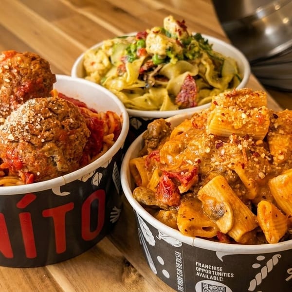 Three bowls of pasta, including spaghetti with meatballs, on a wooden table.