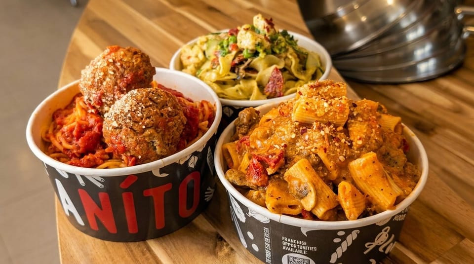 Three bowls of pasta, including spaghetti with meatballs, on a wooden table.