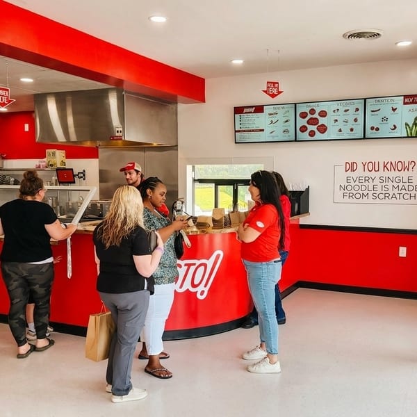 Customers order food at the counter of a modern restaurant with red and white decor.